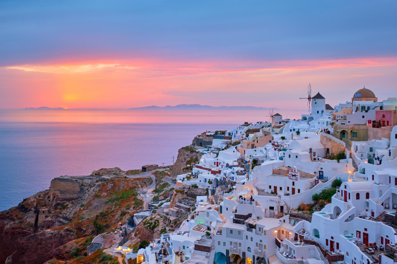 Oia village with traditional white houses and windmills in Santorini island on sunset in twilight, Greece