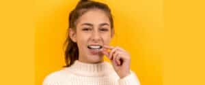 A girl puts a clear aligner into her mouth.