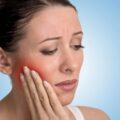 A woman with tooth pain clutches her face.