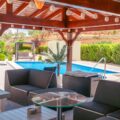 A poolside area in backyard with chairs and a table under a pergola