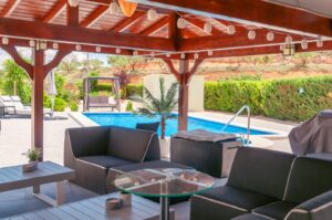 A poolside area in backyard with chairs and a table under a pergola