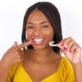 A girl holding a clear aligner and pointing to her teeth.