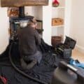 Man examines woodburning stove and chimney with a flue pipe in a home.