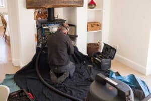 Man examines woodburning stove and chimney with a flue pipe in a home.