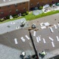 Roofers installing asphalt shingles on a large residential building during a full roof replacement, with underlayment and materials visible.