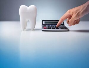 A close-up of a white tooth model next to a calculator, with a hand pressing a button. This visualises the financial cost calculation of dental procedures.